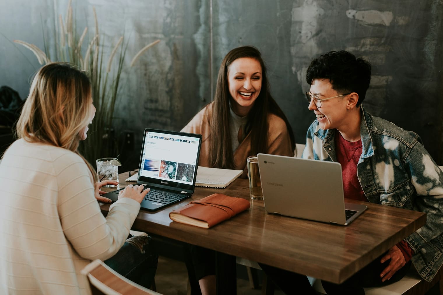 Trois personnes rient autour d'une table de travail, ordinateurs ouverts